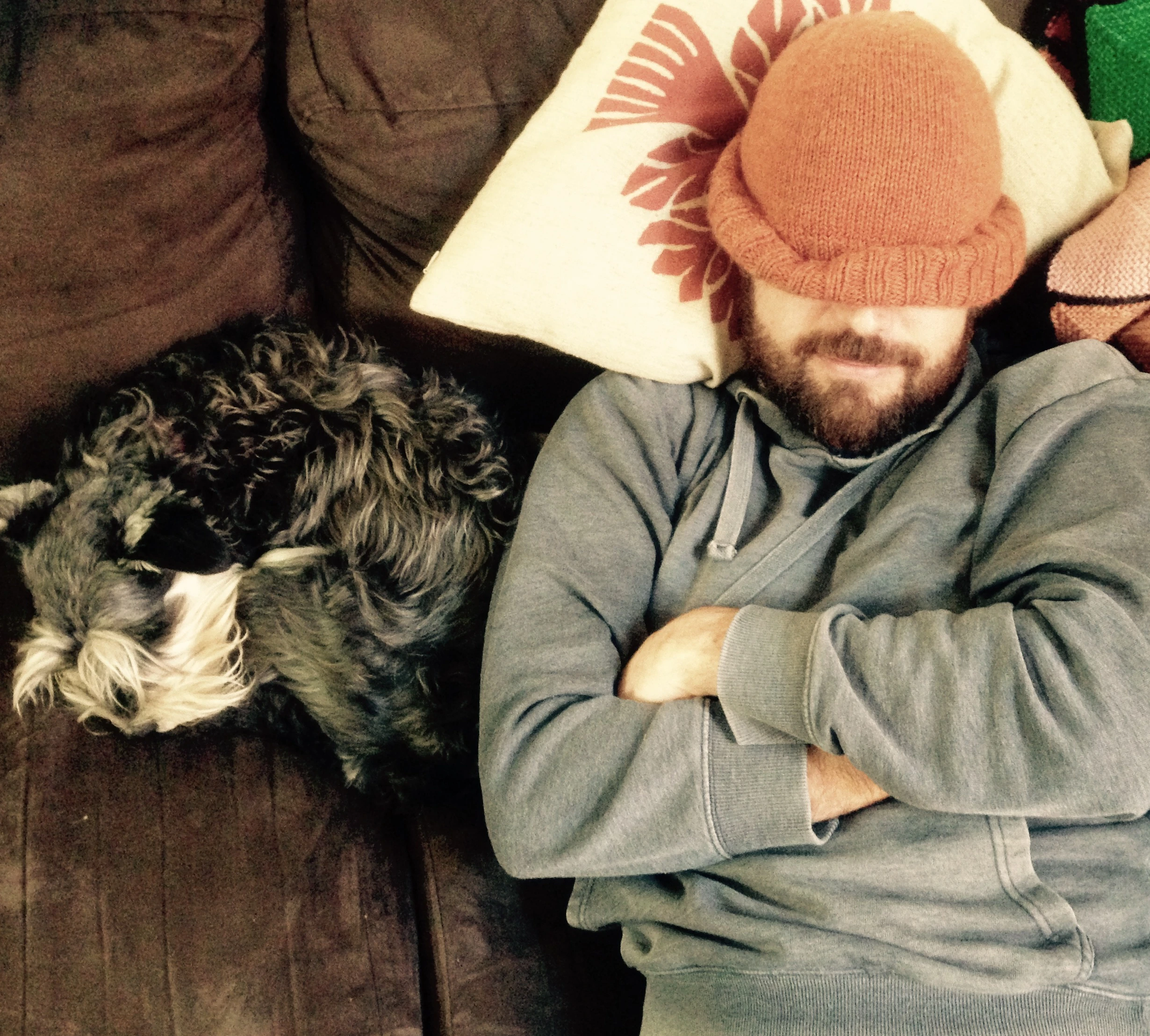 An image of the author sleeping on a couch, beanie down over his eyes, next to a sleeping dog
