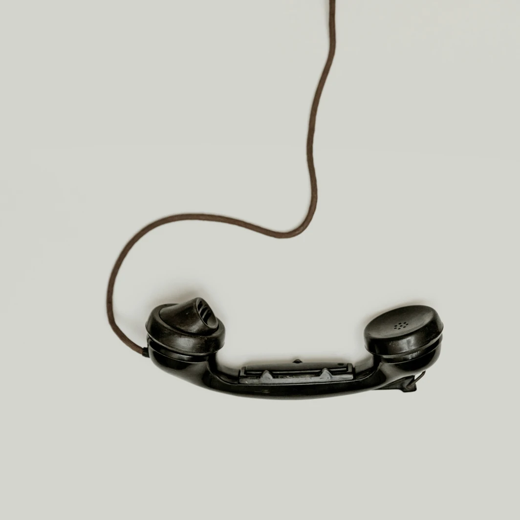 A handset of an old style telephone with a cord against a plain background.